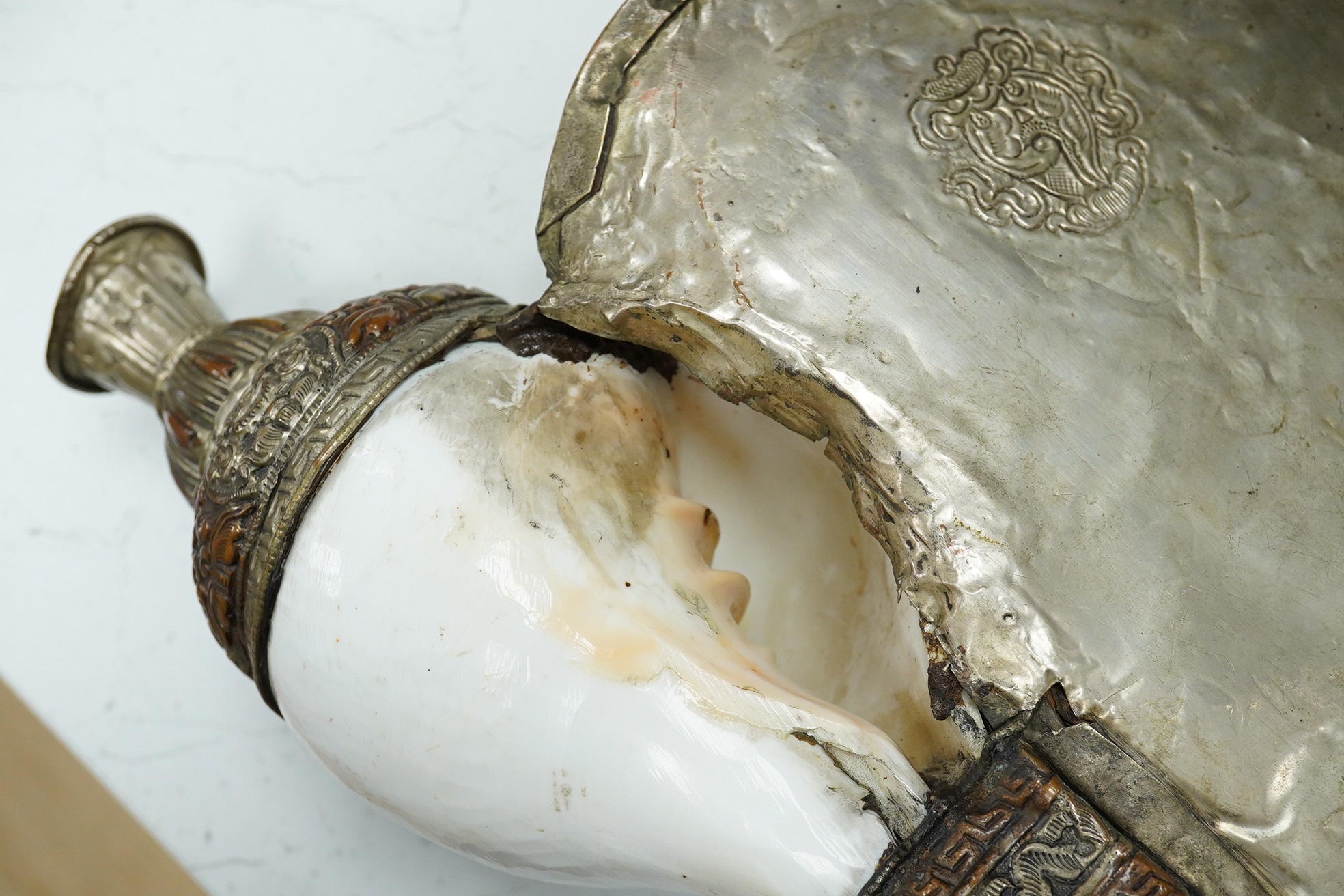 A Tibetan repoussé work cowrie shell trumpet, early 20th century, set with a cabochon, 37cm high. Condition - fair to good